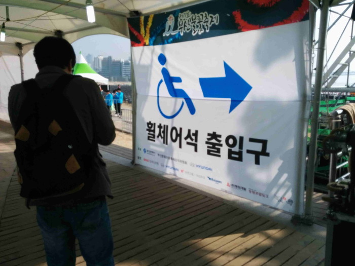 휠체어석 출입구 현수막 앞에 이상훈 팀장이 서 있는 사진