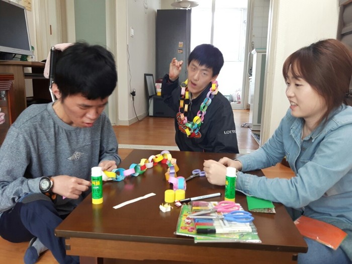 완성된 색종이 띠 목걸이를 반영훈이 목에 걸고 김자운은 마무리를 하고있는 사진