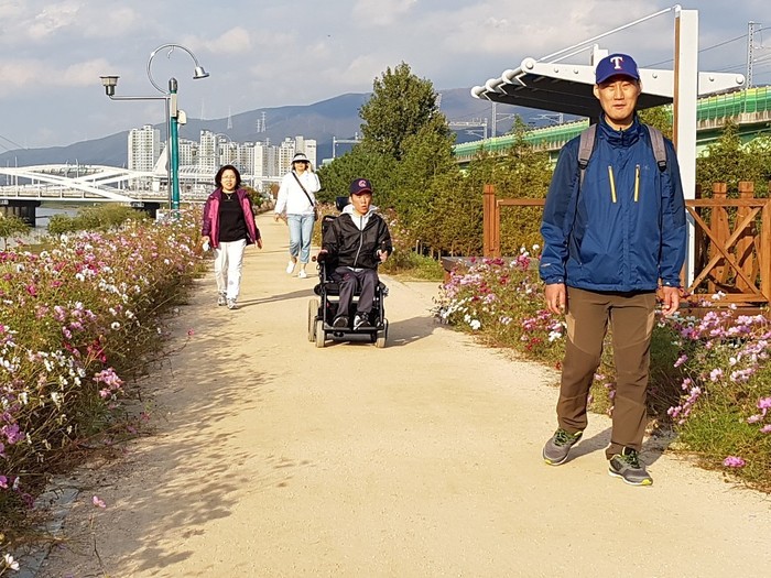 코스모스가 양쪽에 피어있는 길을 걷는 체험 홈 식구들 사진
