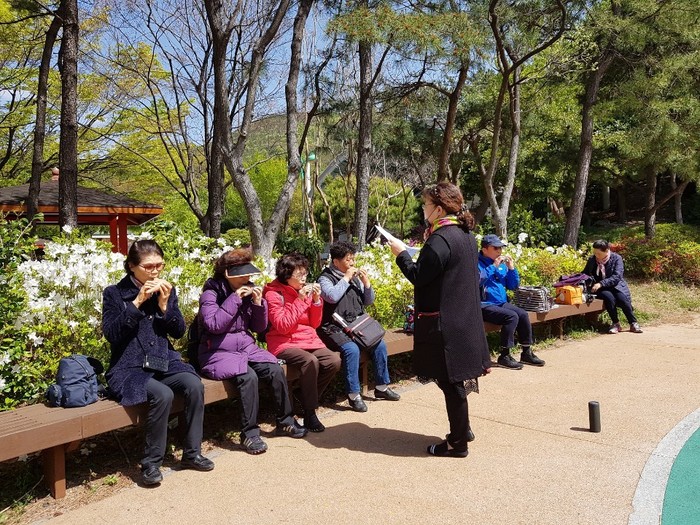 장산 대천 공원 벤치에 앉아 강사님은 악보 보며 소나기 회원들 오카리나 연주 지도 하는 모습 장산 대천 공원 벤치에 앉아 강사님은 악보 보며 소나기 회원들 오카리나 연주 지도 하는 모습